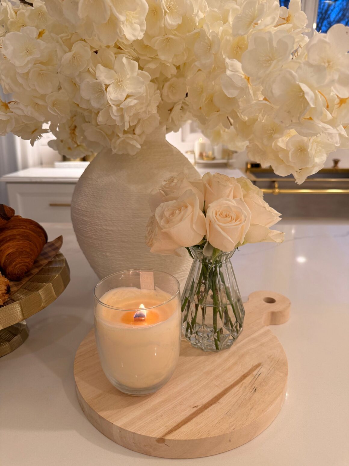 White rose arrangement on wooden board next to candle on kitchen island